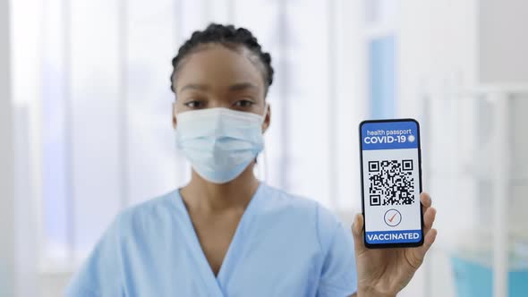 Young Afroamerican Doctor in Medical Mask Showing Smartphone in Her Hand with Mobile Application for alt