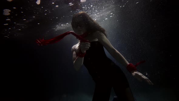 Magic Underwater Shot of Slim Woman Floating in Dark Depth Figure in Darkness Holding Red Whip alt