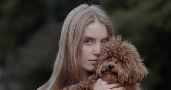 A beautiful girl, blonde, is holding a poodle dog in her hands