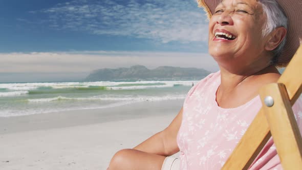 Portrait of mixe race senior woman sitting on subed and smiling at the beach alt