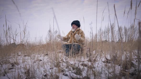 Wide Shot Confident Indigenous Man Meditating Sitting on Winter Day Outdoors on Ice and Snow with alt