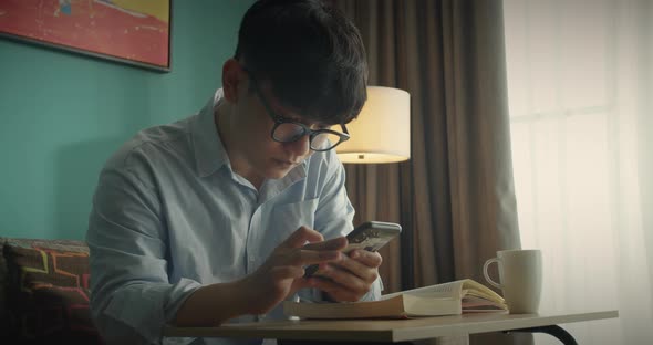 Young Attractive Asian Vietnam Man Busy Work Phone Smart Tephnology on Laptop Learning on Desk Book alt