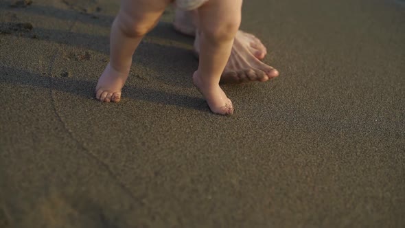 A Little Baby Walking Barefoot on the Sand. Mother Teaches the Child To Walk.