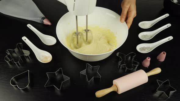 Female hands are mixing dough in bowl with mixer alt
