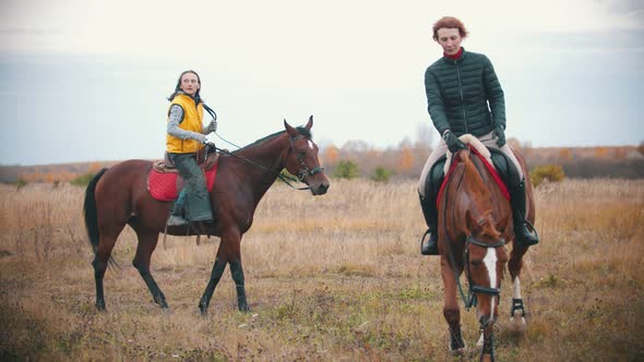Two Women Are Riding Horses Which Are Grazing on the Field alt