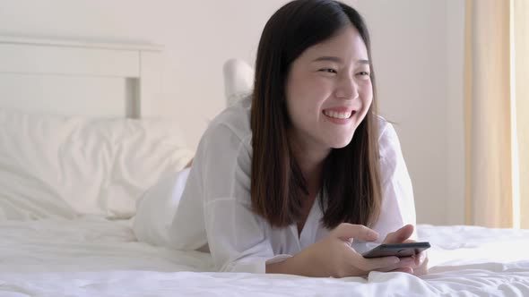 Young woman holding smartphone and lying on the bed alt