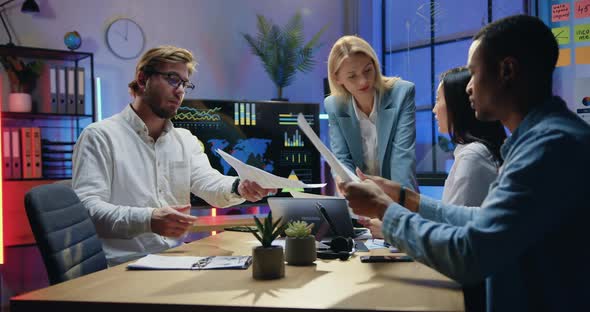 Multicultural Workmates Browsing Paper Reports with Charts During Joint Meeting in Workroom alt