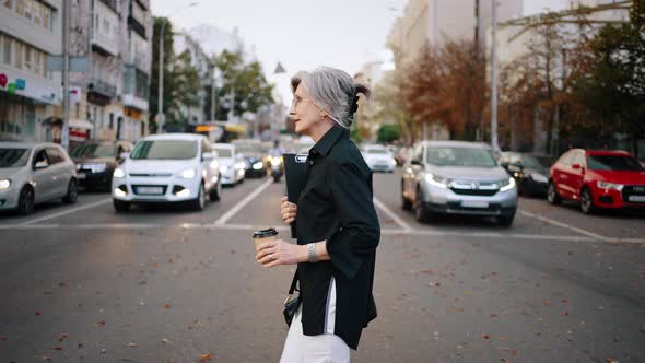 Active Adult Woman Crosses the Street at an Intersection Opposite to the Cars Standing in a Row alt