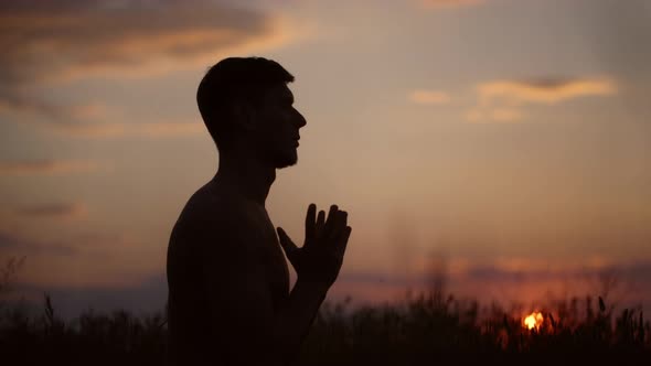 Silhouette of Young Sportive Man Practicing Yoga at Sunset alt