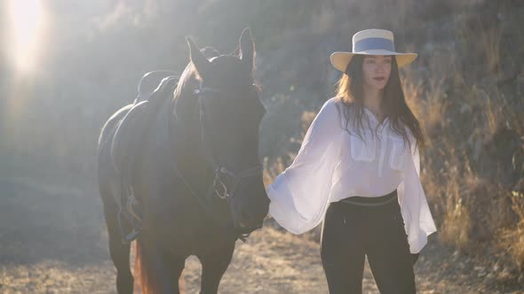Young Slim Woman in White Shirt and Straw Hat Walking in Slow Motion Holding Horse Bridle alt