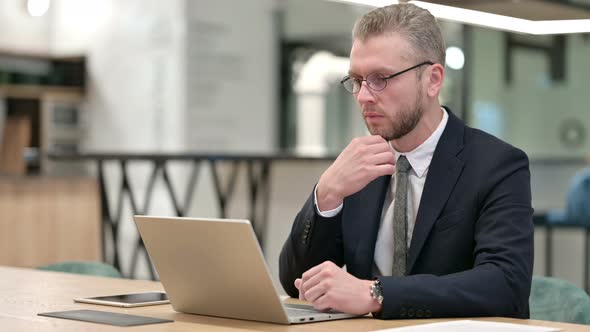 Pensive Businessman Thinking and Working on Laptop in Office  alt