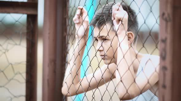 Cinematic Refugee Sad Boy Stands Alone Head Bowed Near the Fence Frustrated Boy Dropped Eyes Regrets