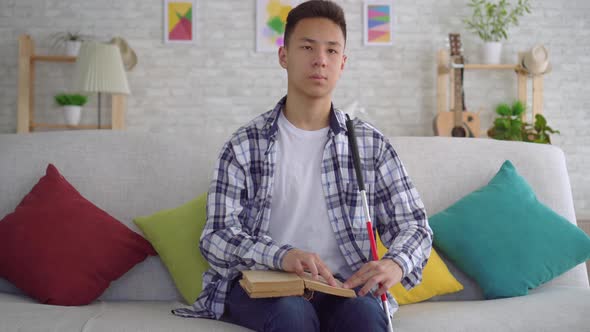 Portrait Blind Asian Young Man Reading a Book of Braille Text Sitting on the Couch in the Living alt