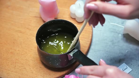 Hand made candles production, female hand mixing melting wax in a pot. Slow motion alt