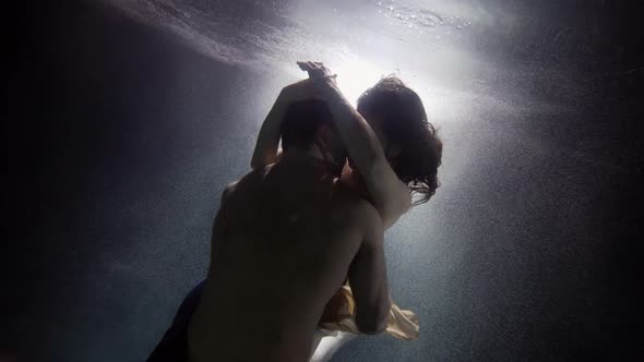 A Man Passionately Embraces and Touches His Woman Underwater Lovers Deep Inside on a Dark Background alt