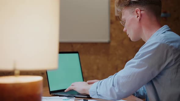 Young Man Actively Typing on the Laptop Working From Home alt