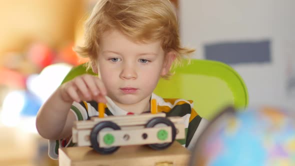 Little blonde boy plays with constructor and builds a vehicle.