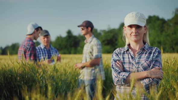 Portrait of a Young Woman Farmer on the Background of the Field and Other Farmers Who Communicate alt
