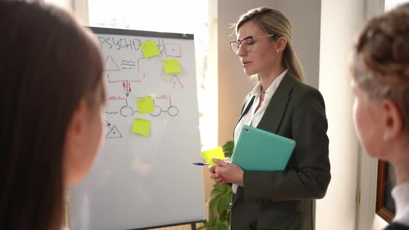 Slim Beautiful Woman in Eyeglasses Standing at Whiteboard Explaining Psychology to Teenage Students alt