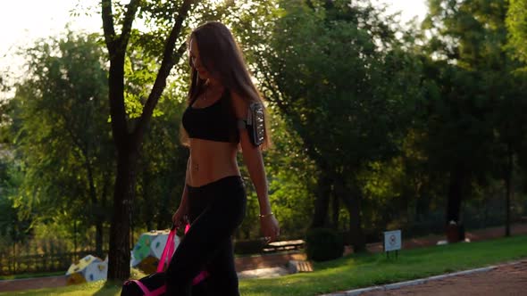 Beautiful Brunette Woman in Short Sport Top and Armband Walking with Sport Bag in the Park alt
