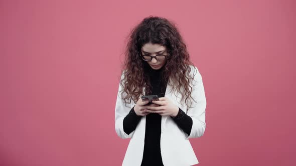 Surprised Young Woman with Curly Hair Typing on the Phone Puzzled alt