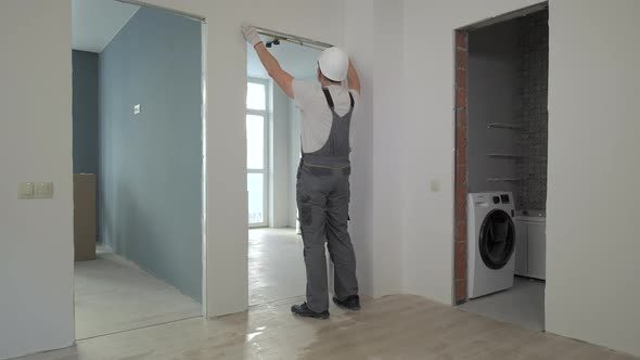 A Builder in Working Uniform Checks the Size and Quality of Doorways in a New Apartment alt