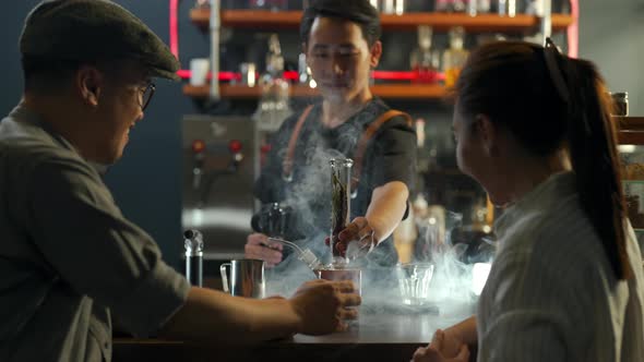 Asian man barista shaking iced black coffee in shaker and pouring in  cocktail glass on bar