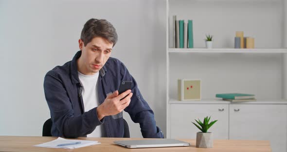 Caucasian Millennial Business Man Adult Young Guy Entrepreneur Sitting in Office Home Holding Phone alt