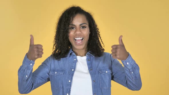 African Girl Gesturing Thumbs Up Isolated on Yellow Background alt