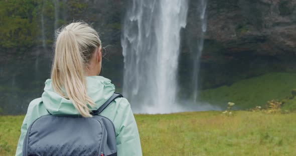 Closeup of Female Traveler Back with Backpack Loking to Beautiful Seljalandsfoss Waterfall Iceland alt