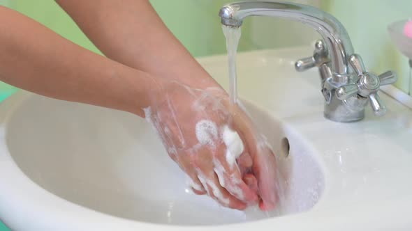 girl washes her hands with soap in the bathroom over the sink
