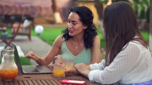 Two Women Sitting at the Outdoors Cafe Talking Sharing News Brunette Girl Showing Something on alt