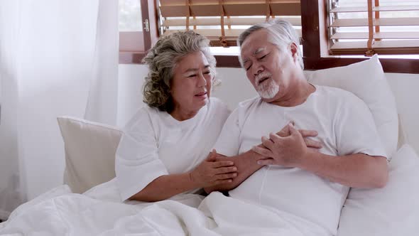 Asian elderly couple in bed, man's heart aches due to heart disease.