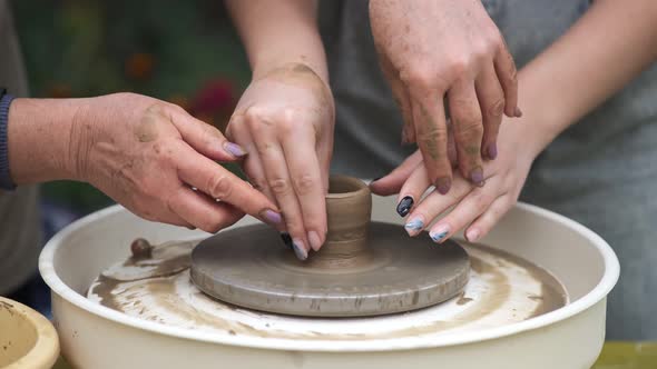An Elderly Female Craftsman Teaches a Young Girl How to Make Pottery on a Potter's Wheel