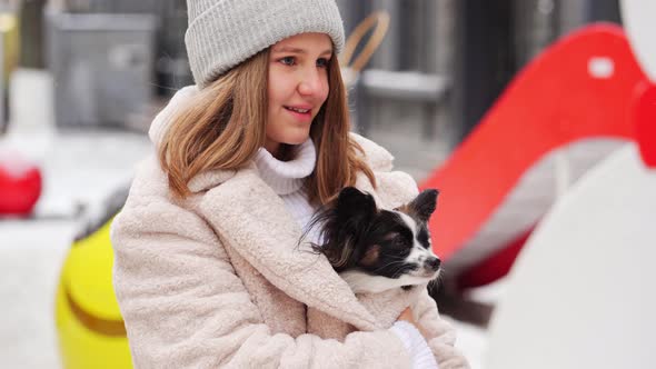 Beautiful Girl with Dog Papillon in Her Arms on Winter Christmas Streets alt