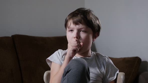 A Sick Little Boy Coughs while Sitting on Chair at Home During a Flu Epidemic
