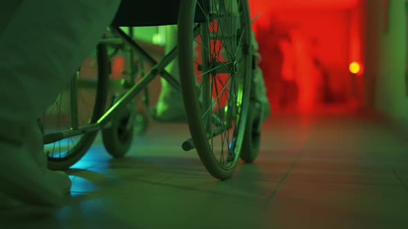 A Paramedic is Driving a Mad Male Patient in Wheelchair Down Corridor in Mental Hospital alt