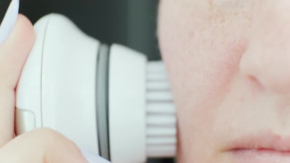 Young woman cleaning face using cosmetic face brush. Facial. Cosmetic procedures.