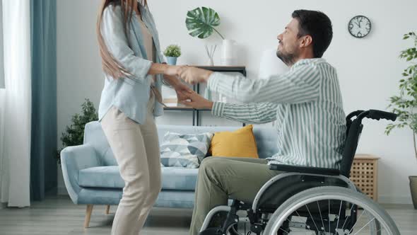 Handicapped Young Man in Wheelchair Dancing with Happy Young Lady at Home alt