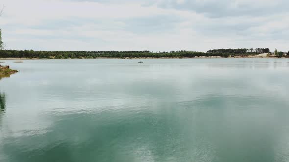 Lonely Man in Boat in the Middle of the Blue Lake Natural Landscape with Pine Tree Forest alt
