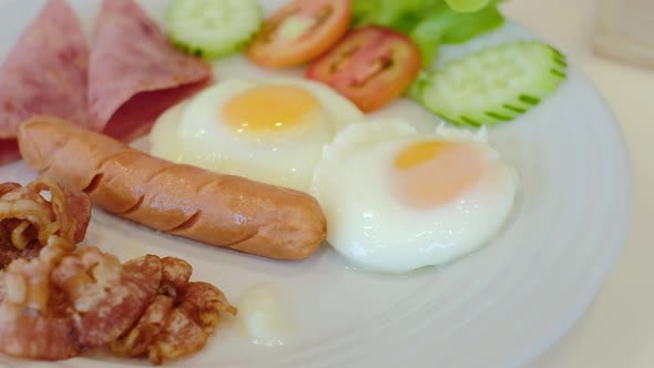 Delicious breakfast with fried egg, bacon, potatoes and sausage on white plate. Close up