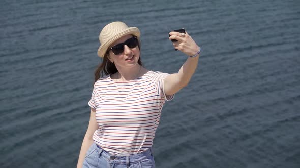 A Young Woman is Filming Herself Against the Backdrop of Water on a Warm Summer Day alt