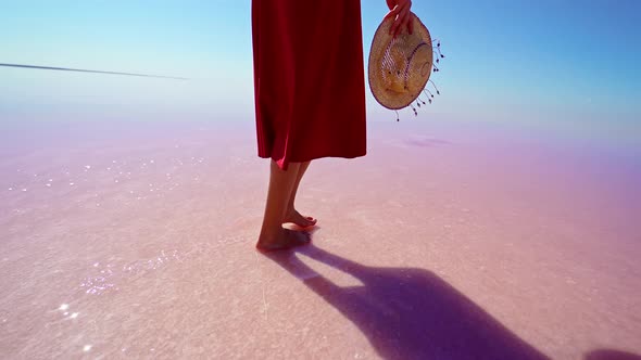 Woman Legs in Red Skirt Walking on Salt White Beach Holding Straw Hat alt