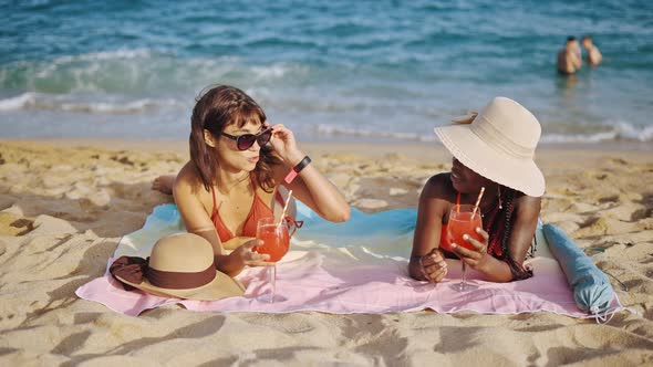 Two Women Lying on Sandy Beach in Swimsuits alt