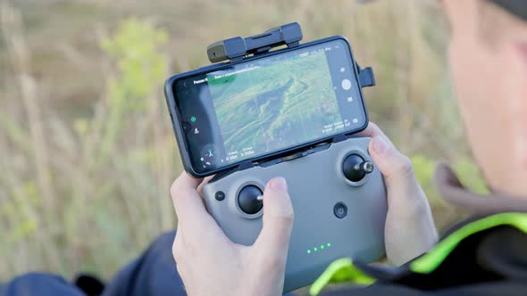 Drone Operator Hands Using Remote Control with Sticks and Cellphone As Monitor at Daylight
