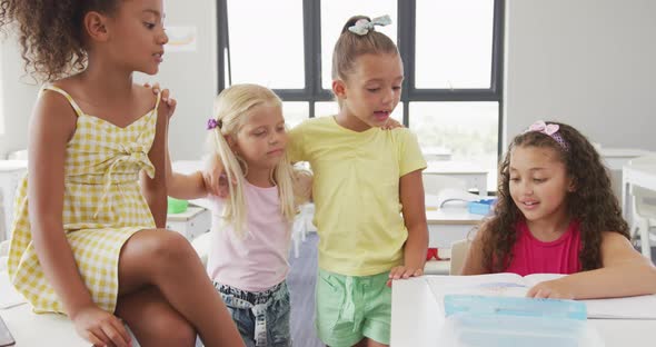 Video of happy diverse girls sitting at school desk, talking and laughing alt