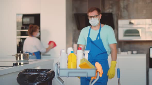 Team of Janitors in Blue Apron Gloves and Mask Disinfecting Kitchen alt