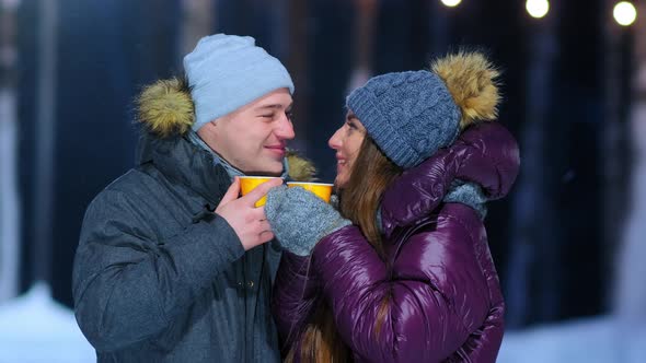 Guy and Girl in Warm Jackets Hold Cups of Hot Drinks on Rink