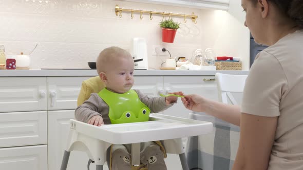 Teaching Baby to Self Feed Using a Spoon Mother Teaches Her 8 Month Old Caucasian Toddler to Eat alt