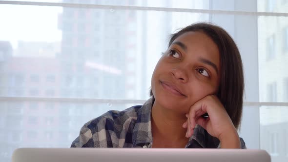 A Beautiful Young Woman is Working at Her Laptop and Looking Dreamily Away